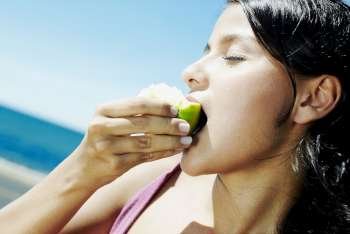 Close-up of a teenage girl eating a green apple with her eyes closed