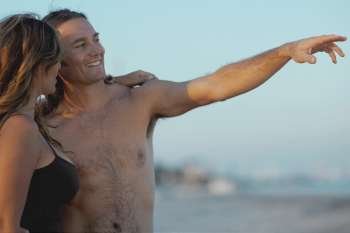 Close-up of a mid adult man standing with his hand raised and a young woman on the beach
