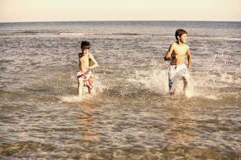 Teenage boy running in water with his brother