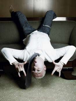 Portrait of a businessman lying upside down on a couch and making I love you signs