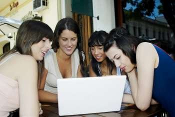 Close-up of two mid adult women and two young women smiling and looking at a laptop