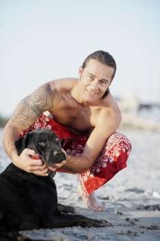 Portrait of a mid adult man crouching and stroking a dog on the beach