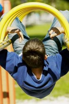 Rear view of a teenage boy hanging upside down on a jungle gym