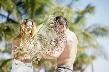 Young woman putting a fishing net over a young man and smiling
