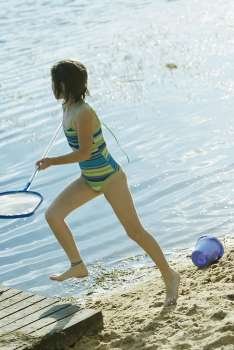 Side profile of a girl holding a fishing net and running at the lakeside