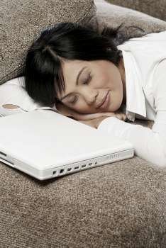 Mid adult woman sleeping on a couch with a laptop in front of her