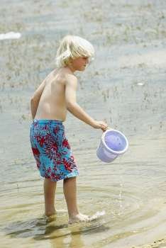 Side profile of a boy holding a sand pail and standing in water