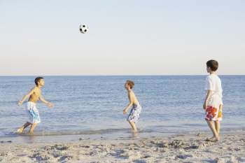 Two boys and a teenage boy playing soccer on the beach