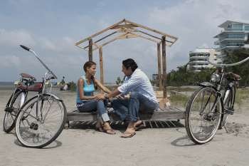 Side profile of a young woman and a mid adult man sitting beside their bicycles