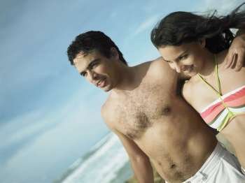 Close-up of a young man with her arm around a teenage girl on the beach