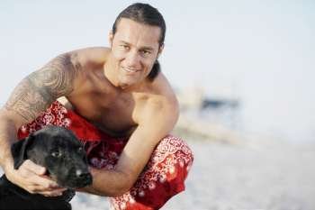 Portrait of a mid adult man crouching on the beach with a dog and smiling