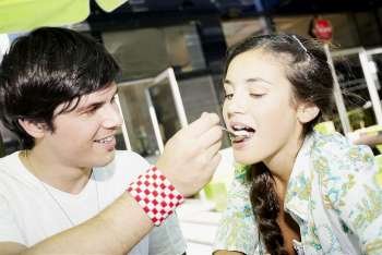 Close-up of a young man feeding ice-cream to a young woman