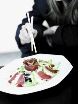 Mid section view of a businesswoman having salad with chopsticks