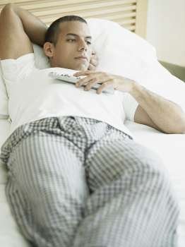 Close-up of a mid adult man lying on the bed and holding a remote control