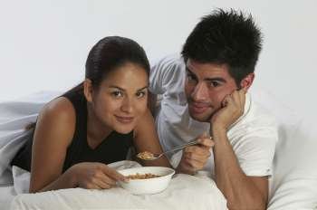 Portrait of a young woman eating a bowl of cereals with a young man beside her