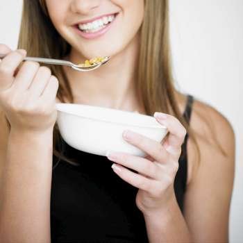 Close-up of a teenage girl holding a bowl and a spoon of corn flakes