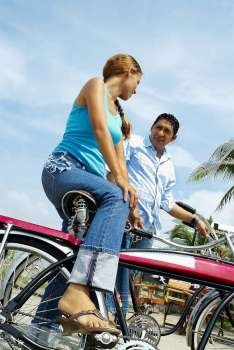 Low angle view of a young woman sitting on a bicycle beside a mid adult man