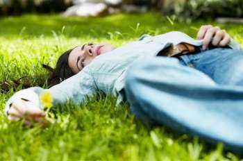 Close-up of a young woman lying on the grass and holding a flower