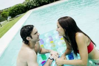 Side profile of a young couple leaning against a pool raft and looking at each other