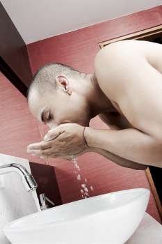 Side profile of a young man washing his face in the bathroom sink