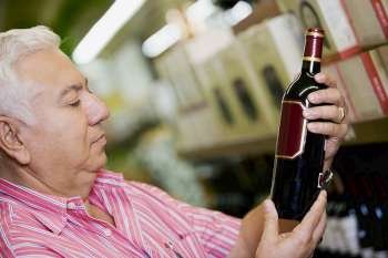 Close-up of a mature man holding a bottle of wine in a supermarket