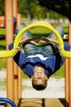 Close-up of a teenage boy hanging upside down on a jungle gym