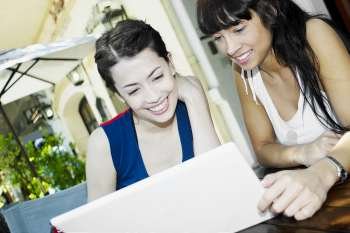 Close-up of a mid adult woman and young woman smiling and using a laptop