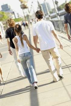 Rear view of a man and a woman holding hands and walking on a walkway