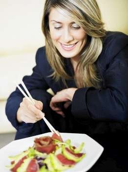 Businesswoman eating salad with chopsticks