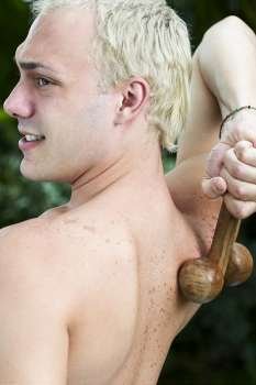 Rear view of a young man massaging his back with a wooden back massager
