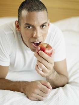 Portrait of a mid adult man lying on the bed and holding an apple