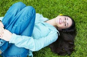 High angle view of a young woman lying on the grass and hugging her knees in the park