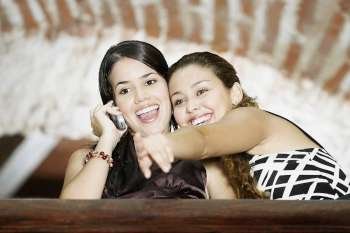 Low angle view of a young woman talking on a mobile phone and pointing forward with her friend
