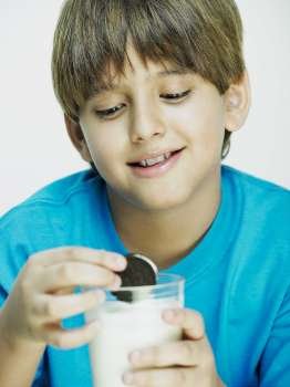 Close-up of a boy dipping cookies into a glass of milk