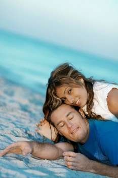 Portrait of a young woman lying on top of a mid adult man on the beach