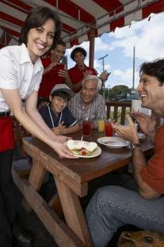 Portrait of a young woman serving dessert to a mid adult man celebrating his son´s birthday in a restaurant