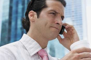 Close-up of a businessman holding a disposable cup and talking on a mobile phone