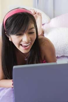 Close-up of a teenage girl lying on the bed and working on a laptop