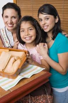 Portrait of a mid adult woman and her two daughters smiling with a tray of breads in the kitchen