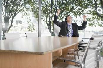 Businessman smiling with arms raised in a conference room