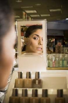 Young woman looking in mirror and sampling cosmetics at beauty supply store