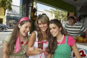 Close-up of a teenage girl holding a mobile phone and standing with her friends