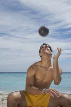 Young man sitting on the beach and playing with a soccer ball