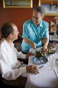 Mature woman serving food to a mature man on the dining table