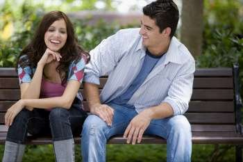 Close-up of a young couple sitting on a park bench and smiling