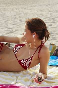 Young woman listening to music while sunbathing on beach