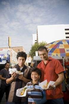 Father and sons eat hot dogs from street vendor