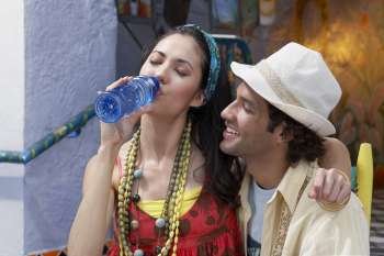 Close-up of a young woman sitting with a young man and drinking water from a water bottle