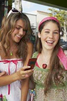 Close-up of a teenage girl holding a mobile phone and standing with her friend