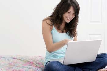 Young woman sitting on the bed and using on a laptop